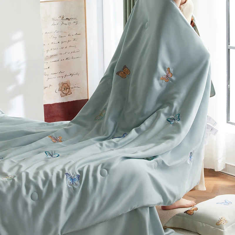 Light blue duvet cover with butterfly embroidery draped over a bed in a bright room.