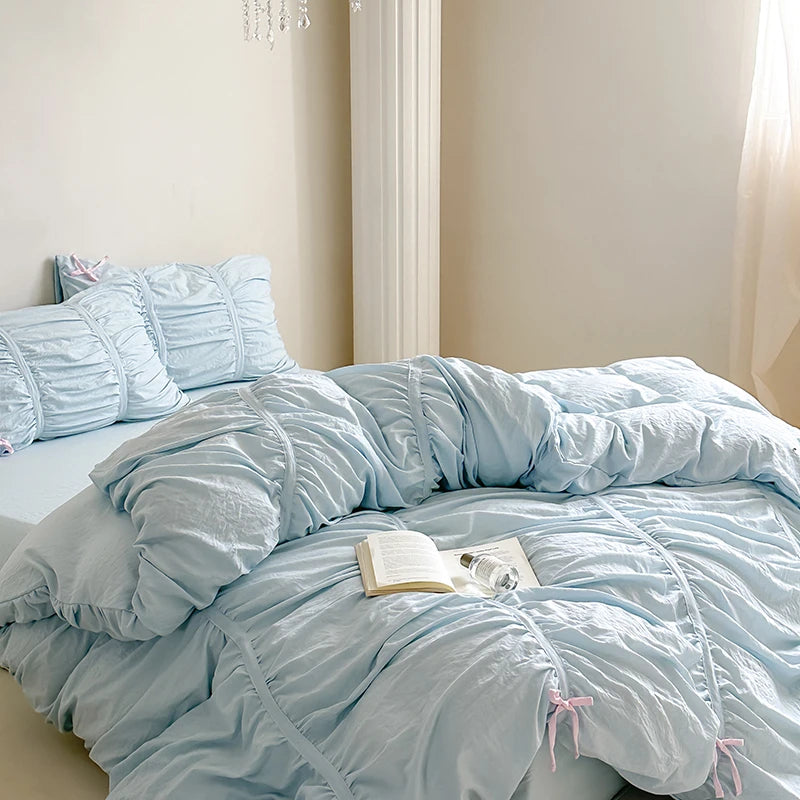 Light blue ruffled comforter set on a bed with pillows and a book.