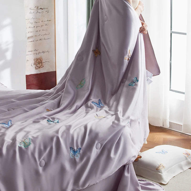 Light purple fabric with butterfly embroidery on a bed in a bright room.