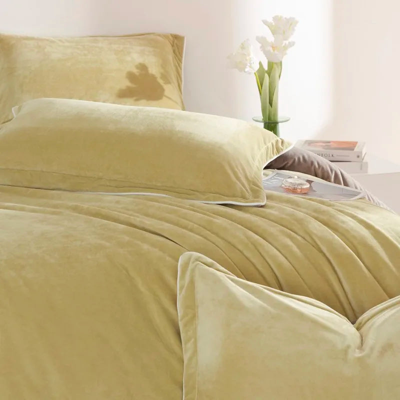 Light yellow bedding set on a bed with pillows and a vase of flowers in the background.