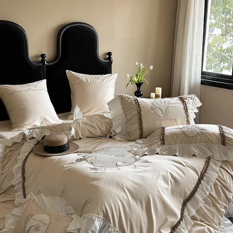 Neatly made bed with decorative pillows and a hat, in a room with a window and vase of flowers.