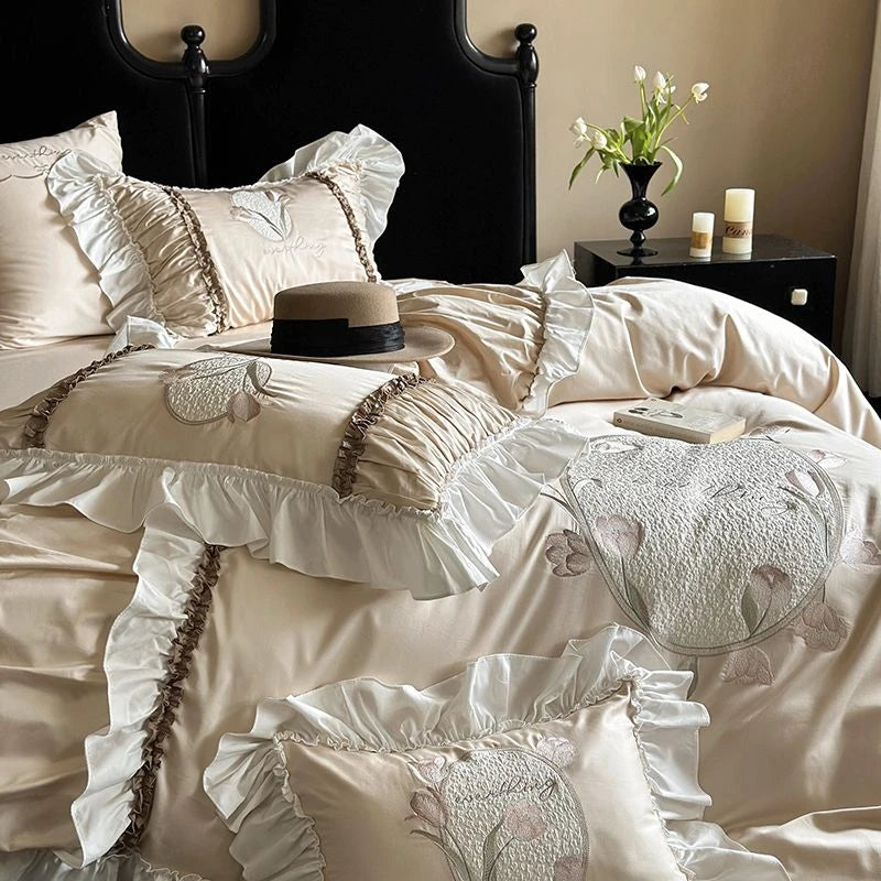 Neatly made bed with decorative pillows and a hat, nightstand with candles and flowers in the background.