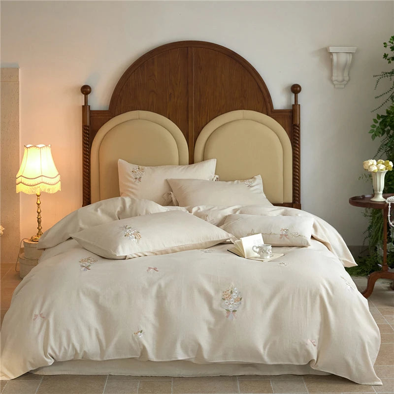 Neatly made bed with white embroidery bedding and wooden headboard in a bedroom setting.