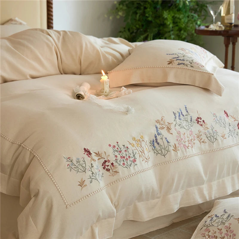 Off white bedding set with floral embroidery on a bed in a bedroom setting.