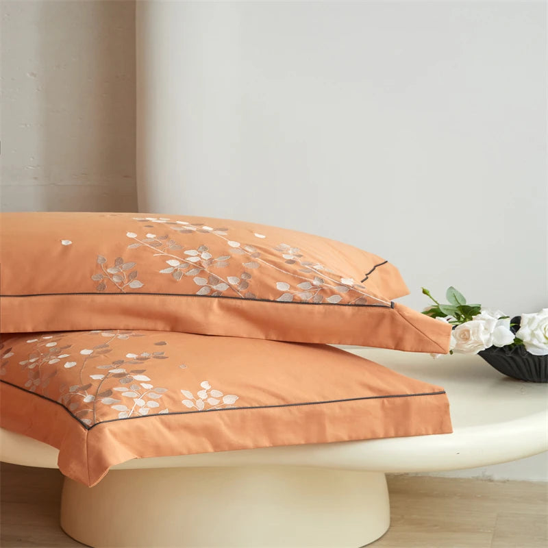 Orange bedding set with floral embroidery on a white surface.