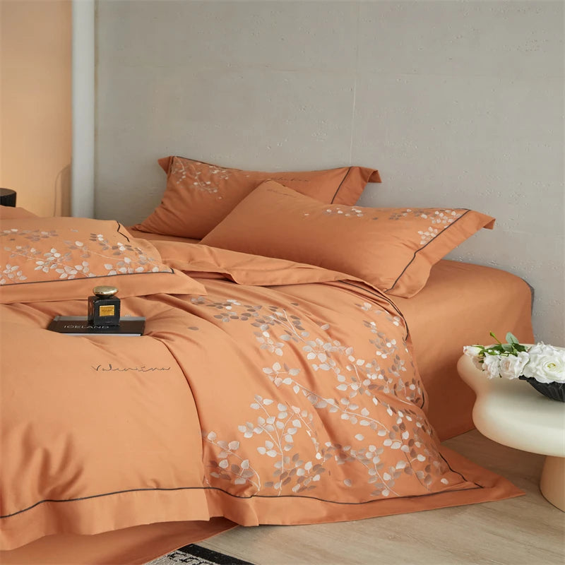Orange bedspread with floral patterns on a bed in a bedroom setting.
