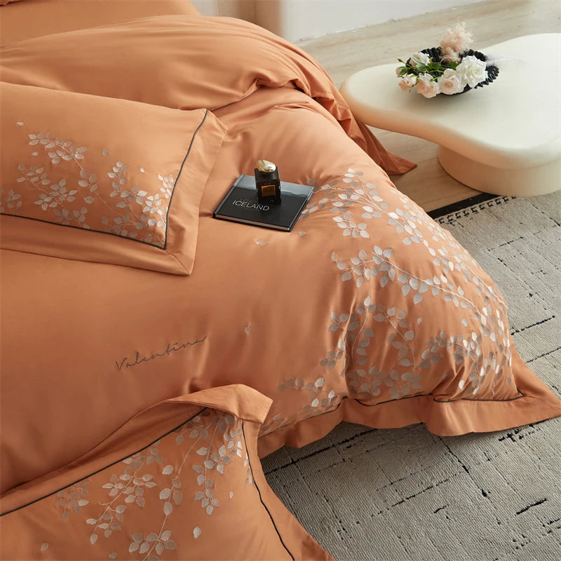 Orange floral bedding set on a bed with a small table and flowers in the background.
