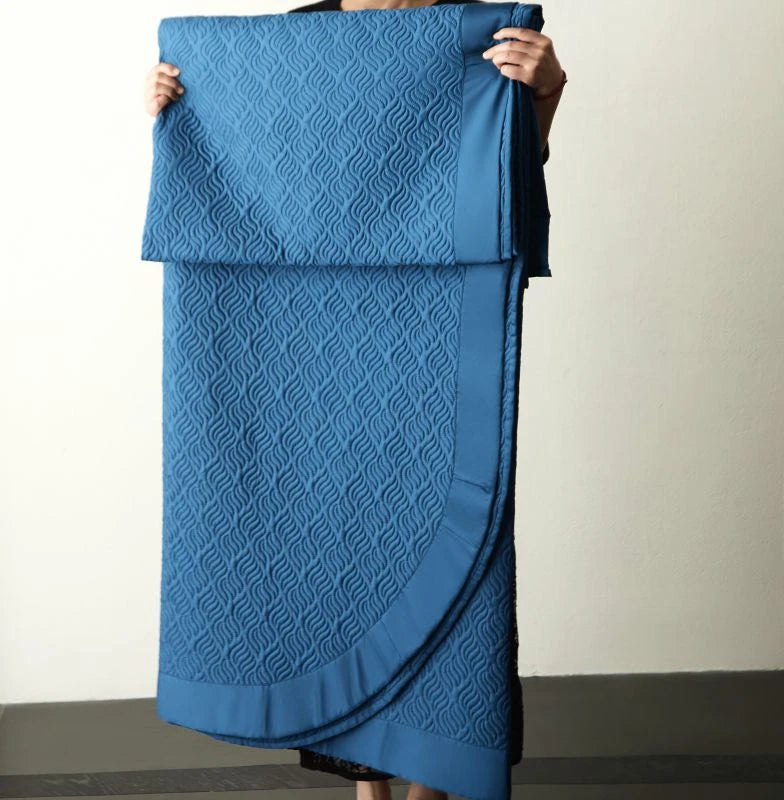 Person holding a blue textured bed spread against a neutral background