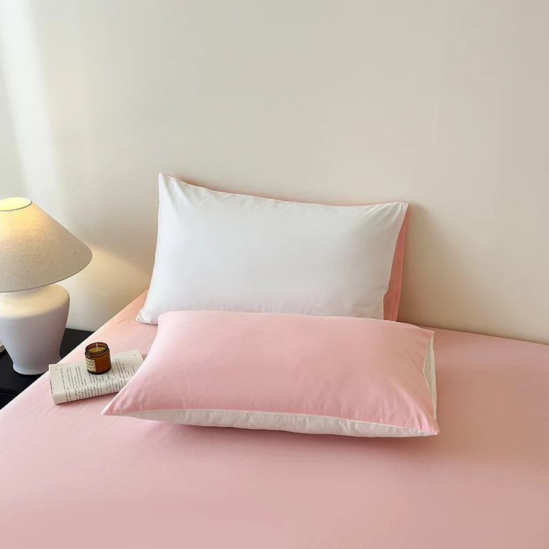 Pink and white pillows on a bed with a lamp in the background