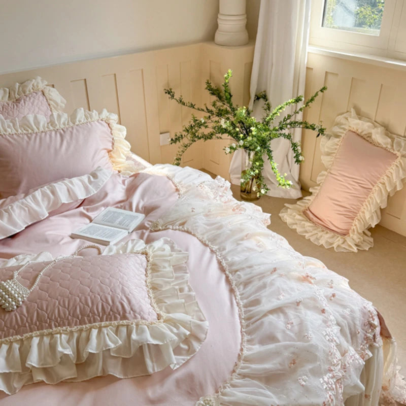 Pink and white ruffled bedding with a vase of flowers on a bed.