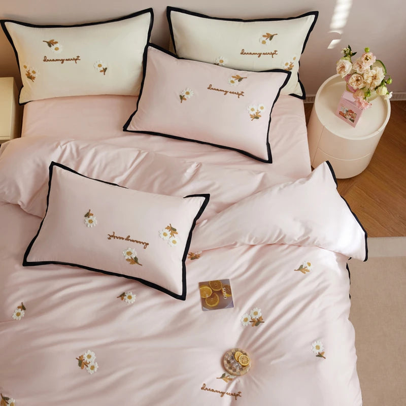 Pink bedding set with embroidered designs on a bed in a bedroom.