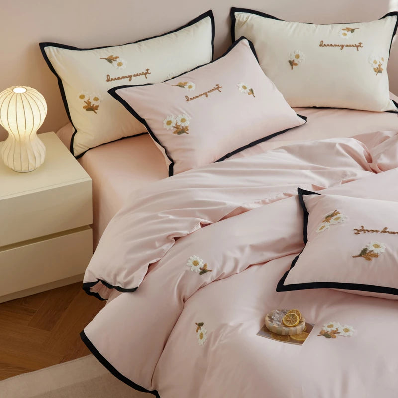 Pink bedding set with embroidered designs on a bed in a bedroom setting.