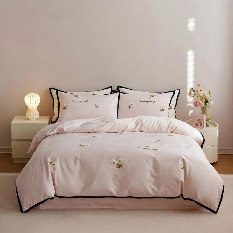Pink floral embroidered bedding set on a bed in a bedroom setting.