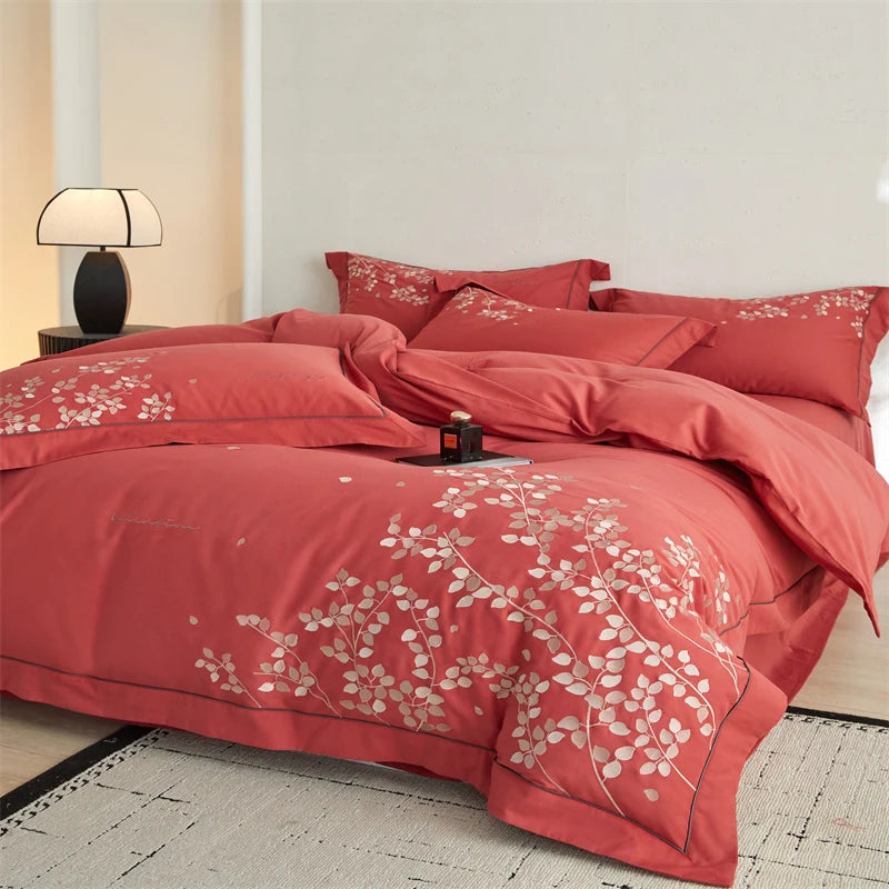 Red floral bedding set on a bed in a bedroom with a lamp and nightstand.