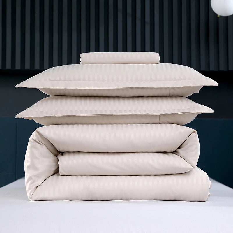 Stack of beige bedding including a duvet and pillows on a dark background