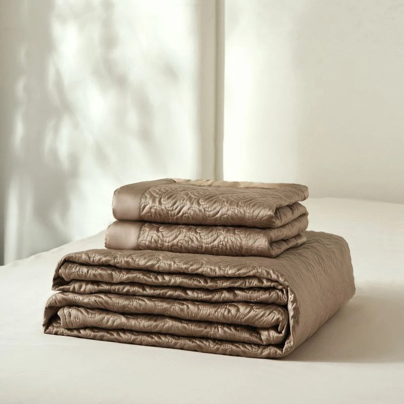 Stack of brown quilted bedding set on a white surface with a neutral background