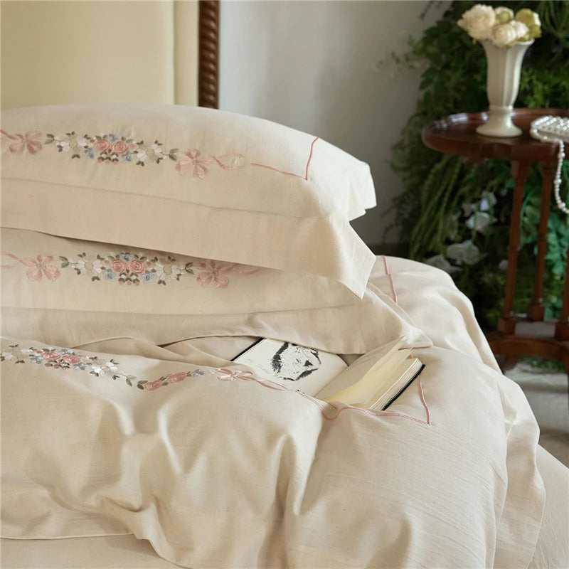 Stack of embroidered bedding with a floral pattern in a bedroom setting.