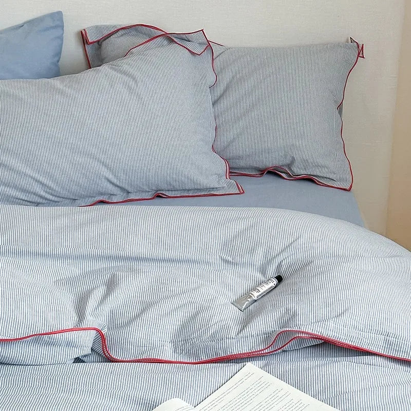 Striped bed sheets and pillows with red piping on a bed.