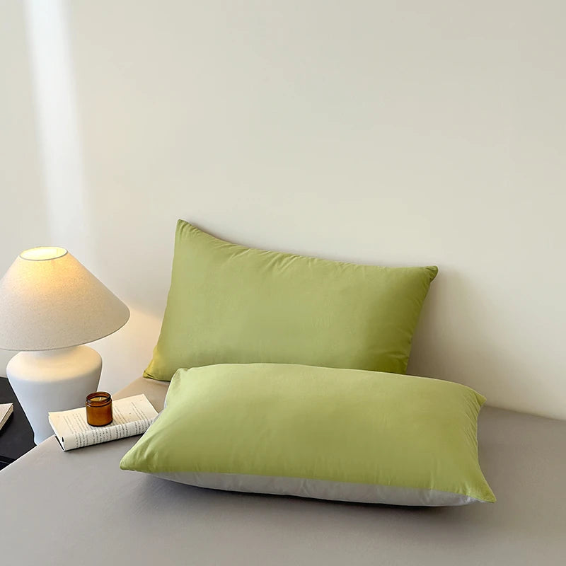Two green pillows on a bed next to a nightstand with a lamp and small jar.