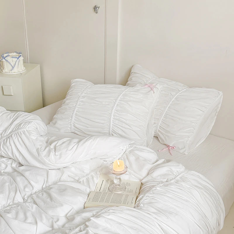White bedding set on a bed with a candle and book in the foreground.