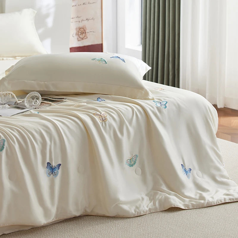 White bedding set with butterfly embroidery on a bed in a bright room.