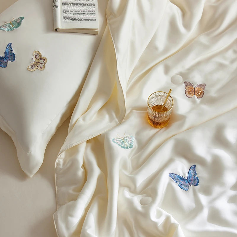White bedding set with embroidered butterflies and a glass of honey on a light surface.