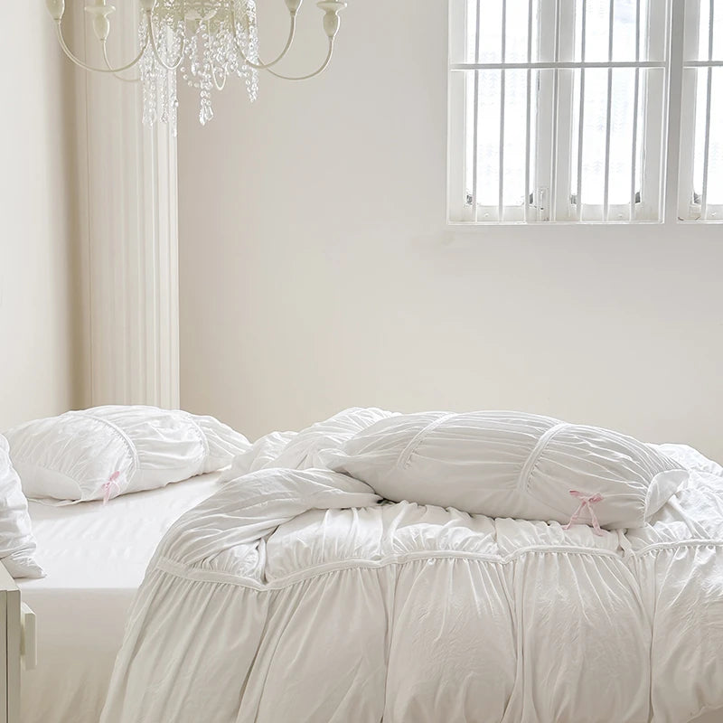 White comforter on a bed in a bright bedroom with a chandelier.