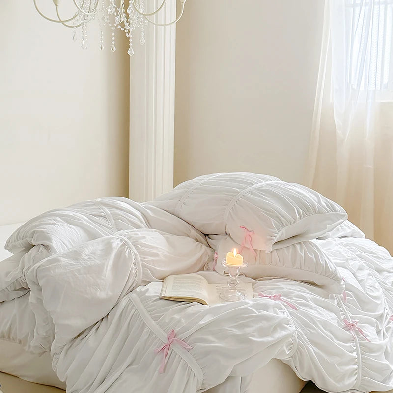 White comforter on a bed with a candle and book in a softly lit room.