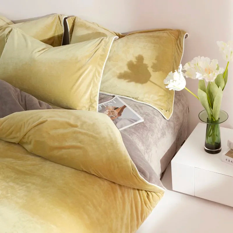 Yellow bedding and pillows on a bed with a side table and flowers.
